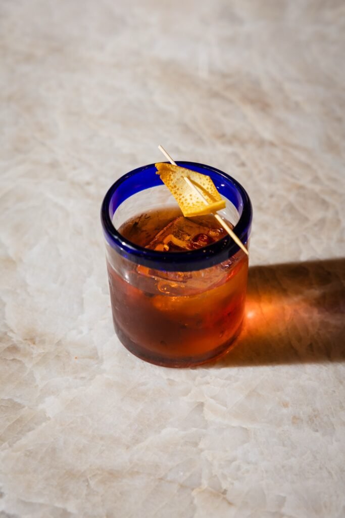 El Padrino cocktail with a large ice cube and orange peel in a blue-rimmed rocks glass